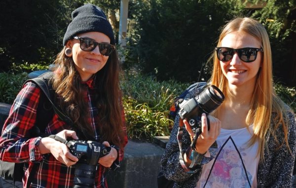 Zwei junge Frauen mit Sonnenbrillen und Kameras in den Händen