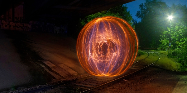 Ein kreiselnder Feuerball auf Schienen, beleuchtet von einer einzelnen Straßenlaterne