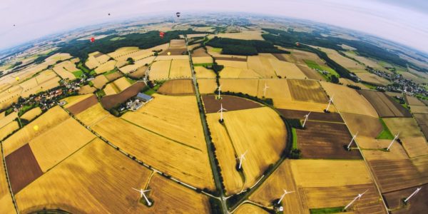 Blick mit Fischaugen-Effekt aus einem fahrenden Ballon auf eine ländliche Gegend mit Windkraftwerken. Am Horizont sind Ballone zu sehen.