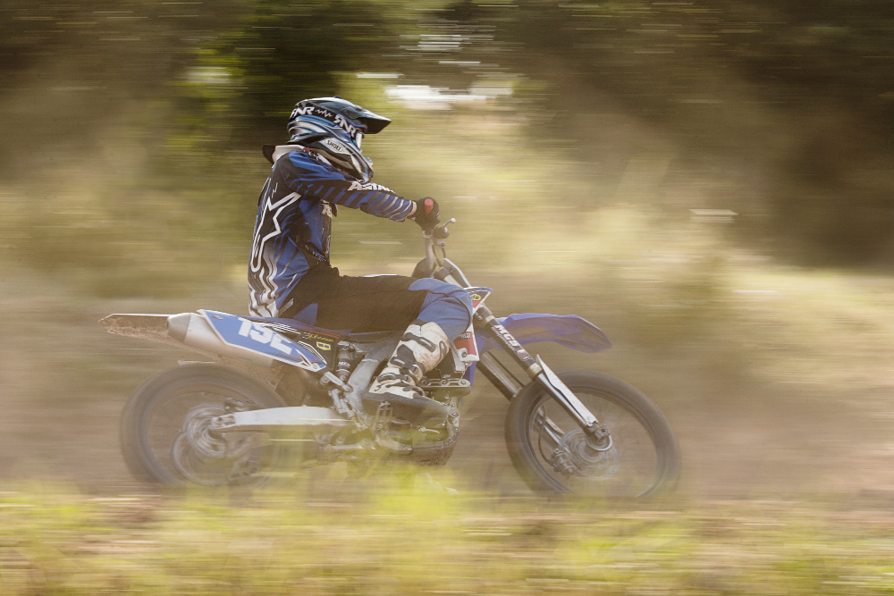 Ein Motocross-Fahrer wischt durchs Bild. Die Aufnahme wurde mitgezogen, das heißt das Motorrad ist scharf, der Vorder- und Hintergrund nicht. 