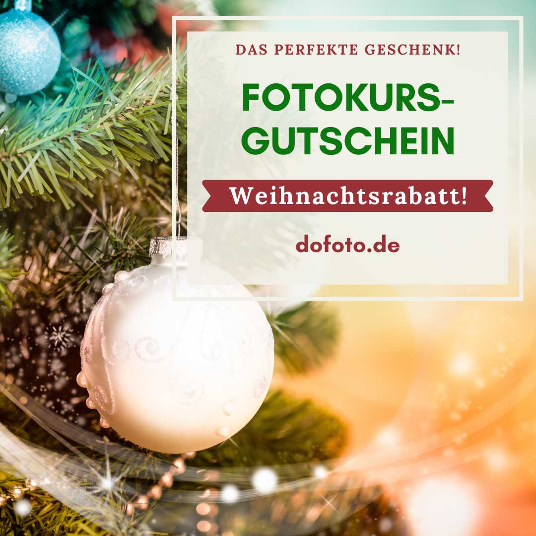 Unser Fotokurs-Gutschein zu Weihnachten. Es ist zu sehen: Ein Teil des Weihnachtsbaums mit iener großen, weißen Kugel und ein paar kleinere goldene Ketten mit Kugelelementen im unscharfen Hintergrund.